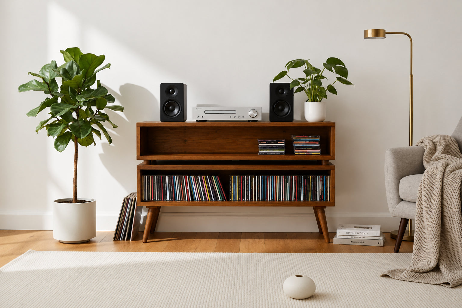 A mid-century modern wooden media console styled in a bright living room with plants, speakers, a record player, a floor lamp, and a light gray armchair.