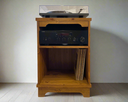Wooden record player stand with vinyl records and electronic equipment against a plain wall.
